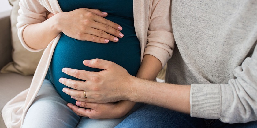 En gravid kvinde holder på sin mave. Manden er ved siden af og gør det samme.